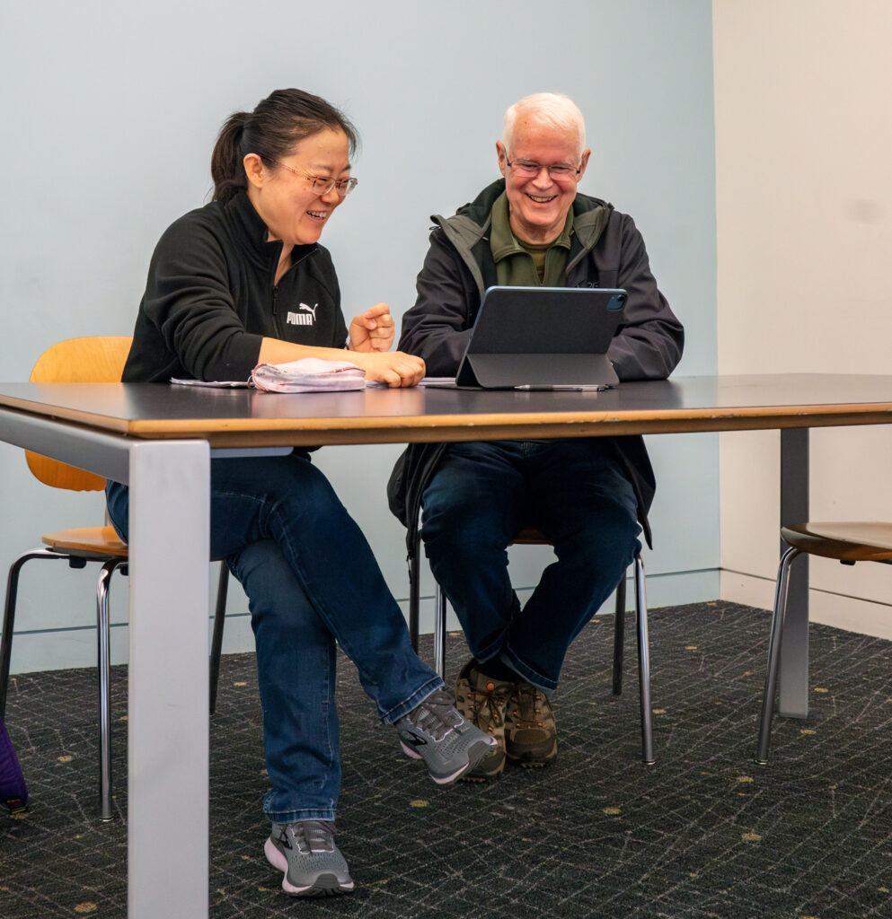 Bob and Junyi watch a video on an iPad during an adult education session. 