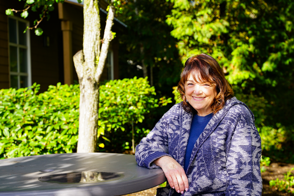 Cindy smiles at the camera while sitting at an outdoor table in the sun.